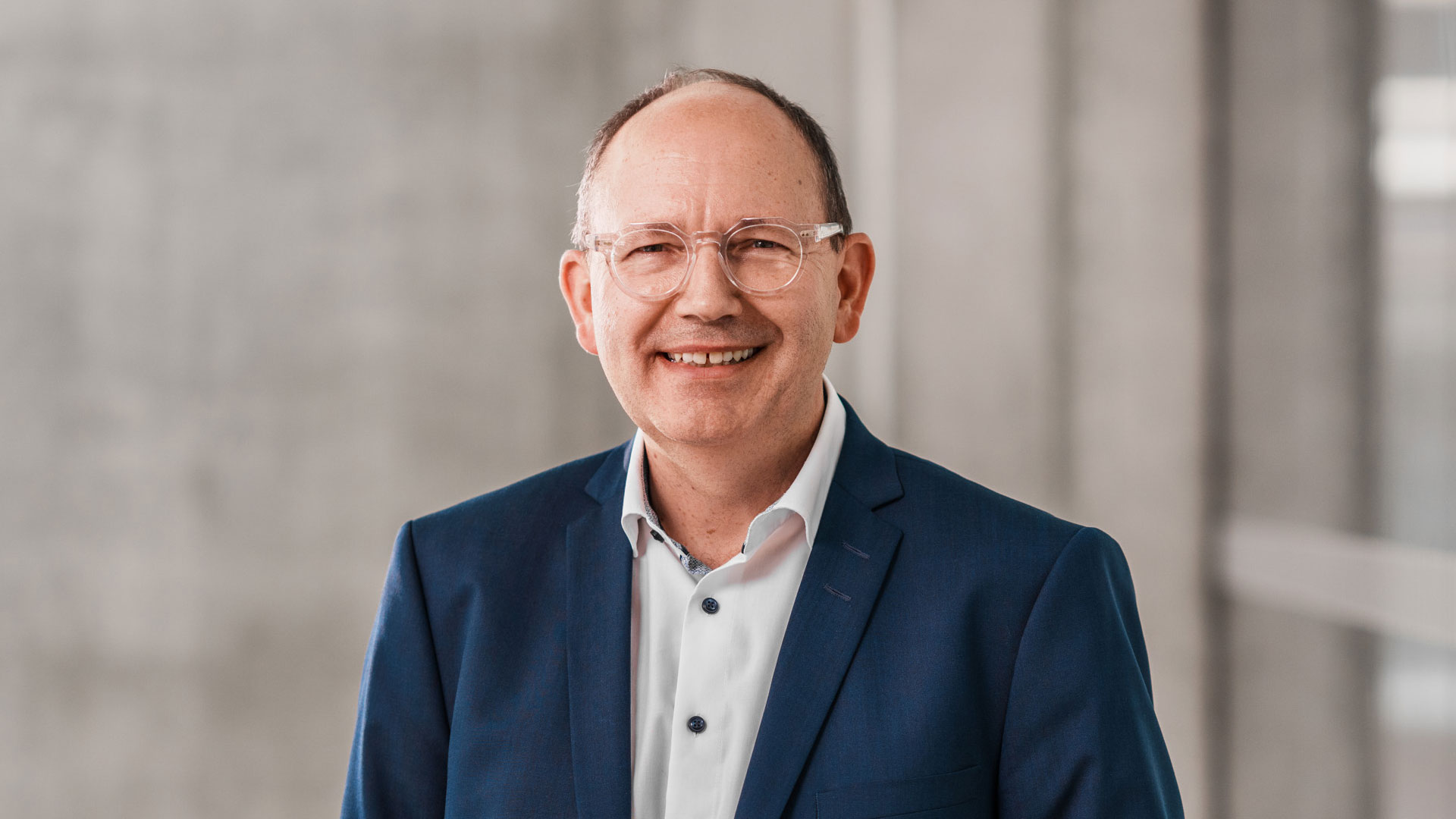 Portrait von Christian Specht vor einer Betonwand mit Glasfassade.